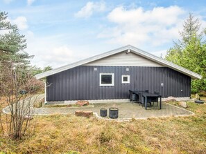 A modern building with a dark exterior, a sloped roof, and a paved patio area with outdoor furniture. - Secluded Holiday Home in Henne near Beach (Henne)