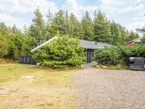 A rustic cabin with a gravel driveway, surrounded by dense evergreen trees. - Secluded Holiday Home in Henne near Beach (Henne)
