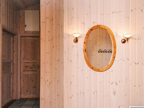 Una habitación con paneles de madera, un espejo redondo y dos luces fijadas a la pared.
