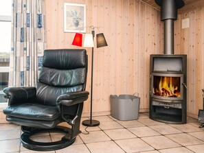 A room with a black leather chair, a floor lamp, a wood-burning stove, and a framed picture on the wall.