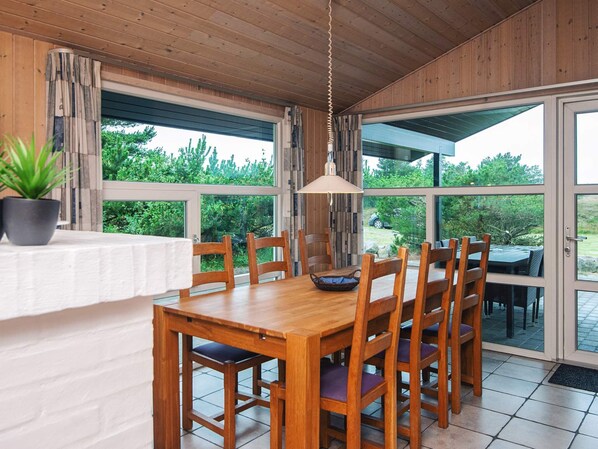 Un comedor de madera con una mesa y sillas, ventanas amplias y una planta en maceta.