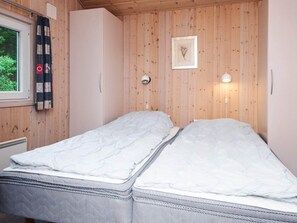 Una cama individual con colchón blanco y ropa de cama gris en una habitación con paredes de madera y una ventana con cortinas.