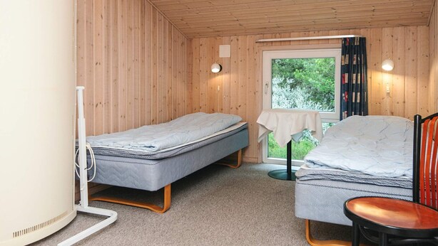 A compact room with two single beds, a small table, a chair, and a window with curtains. - Secluded Holiday Home in Henne near Beach (Henne)