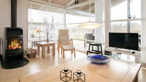 Uma sala de estar moderna com uma lareira a lenha, uma TV e uma janela grande com vista para um terraço.