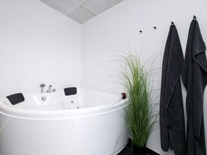 Une salle de bain moderne avec une baignoire blanche, une plante en pot et deux serviettes accrochées au mur.