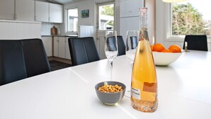 A modern kitchen with white cabinets, a dining table with chairs, a bottle of rosé wine, a bowl of nuts, and a bowl of oranges. - Peaceful Holiday Home in Blavand Denmark With Terrace (Blavand)