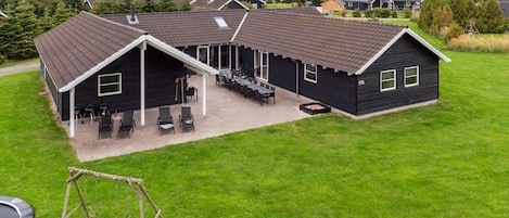 A residential building with a covered patio area, outdoor seating, and a swing set.