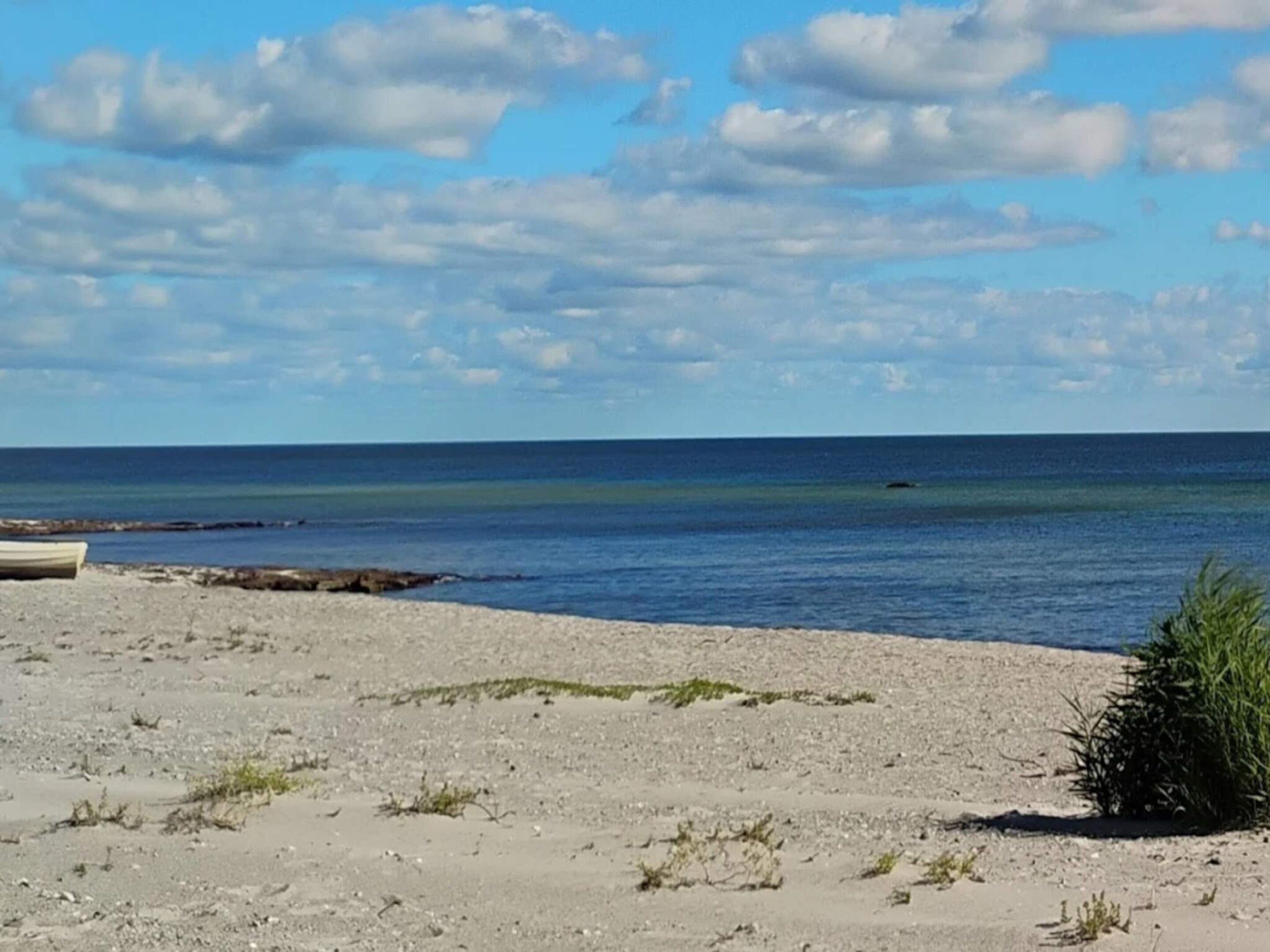 Una playa con un bote, cielo despejado y mar tranquilo.