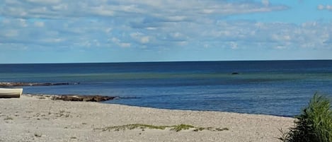 Una playa con un bote, cielo despejado y mar tranquilo.