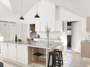 A modern kitchen with white cabinetry, a central island with stools, pendant lighting, and a view to the outside. - 5 Star Holiday Home in Idestrup (Idestrup)