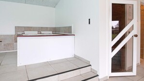 A modern kitchen with a white countertop and a built-in stove. There are steps leading to a glass door with a wooden frame. - 5 Star Holiday Home in Hals (Hals)