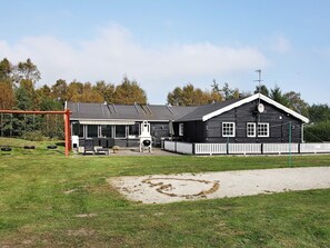A black wooden building with a white picket fence, a covered outdoor seating area, and a swing set.