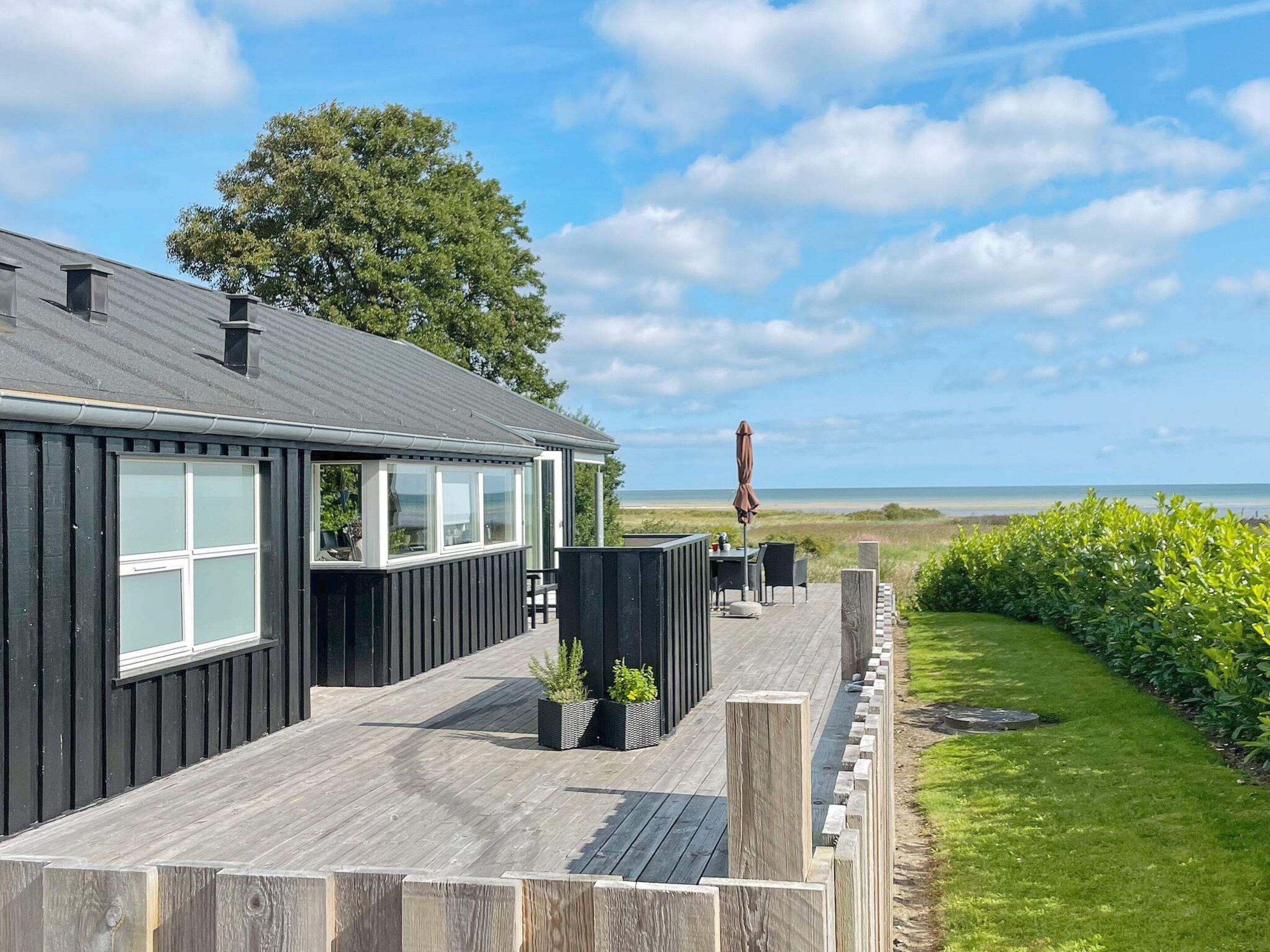 A wooden deck with a view of the sea, a covered outdoor seating area, and a grassy landscape.