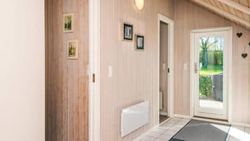 Un pasillo con paredes de madera, un radiador blanco y una puerta que da al exterior.