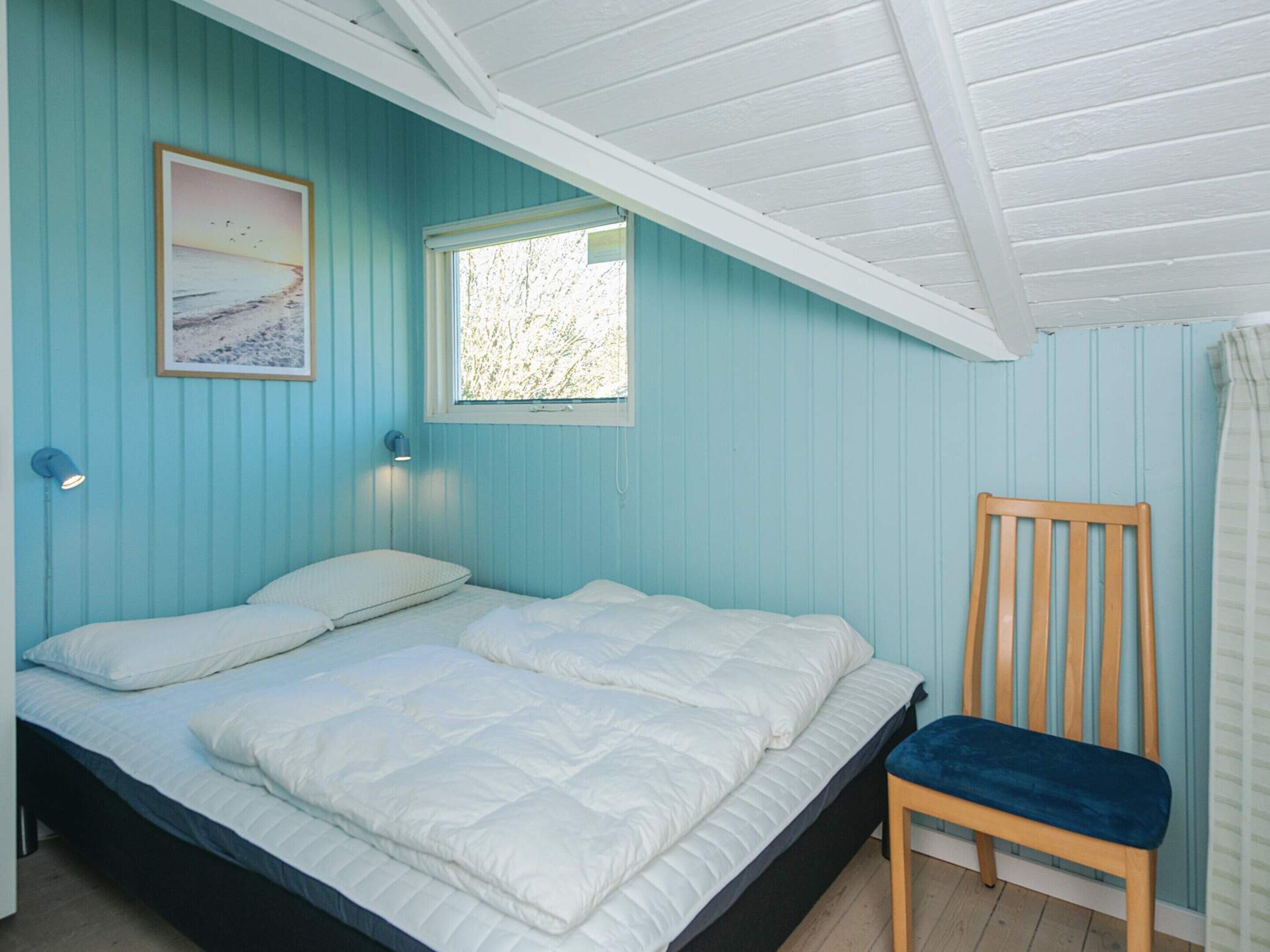 Et soveværelse med en seng, en stol, et vindue og en vægmonteret lampe.