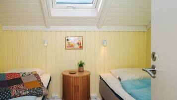 A room with two beds, a small round wooden table, a potted plant, a framed picture on the wall, and a skylight above.