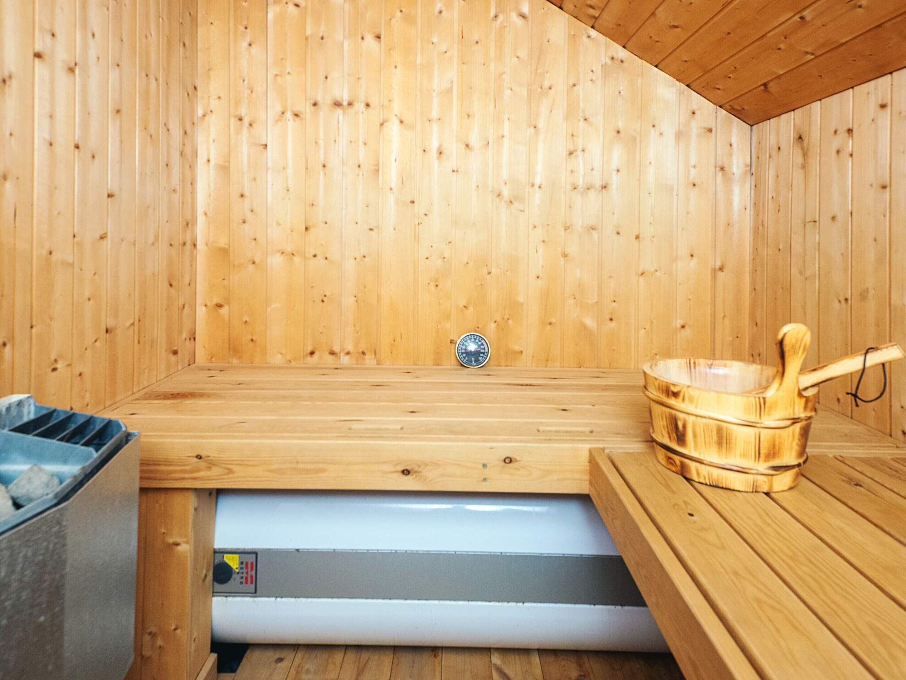 A sauna room with wooden walls, a bench, a bucket, and a control panel.