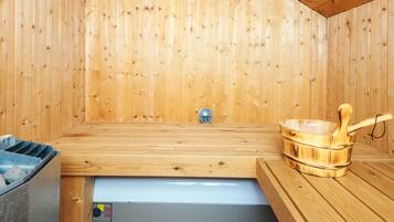 A sauna room with wooden walls, a bench, a bucket, and a control panel.