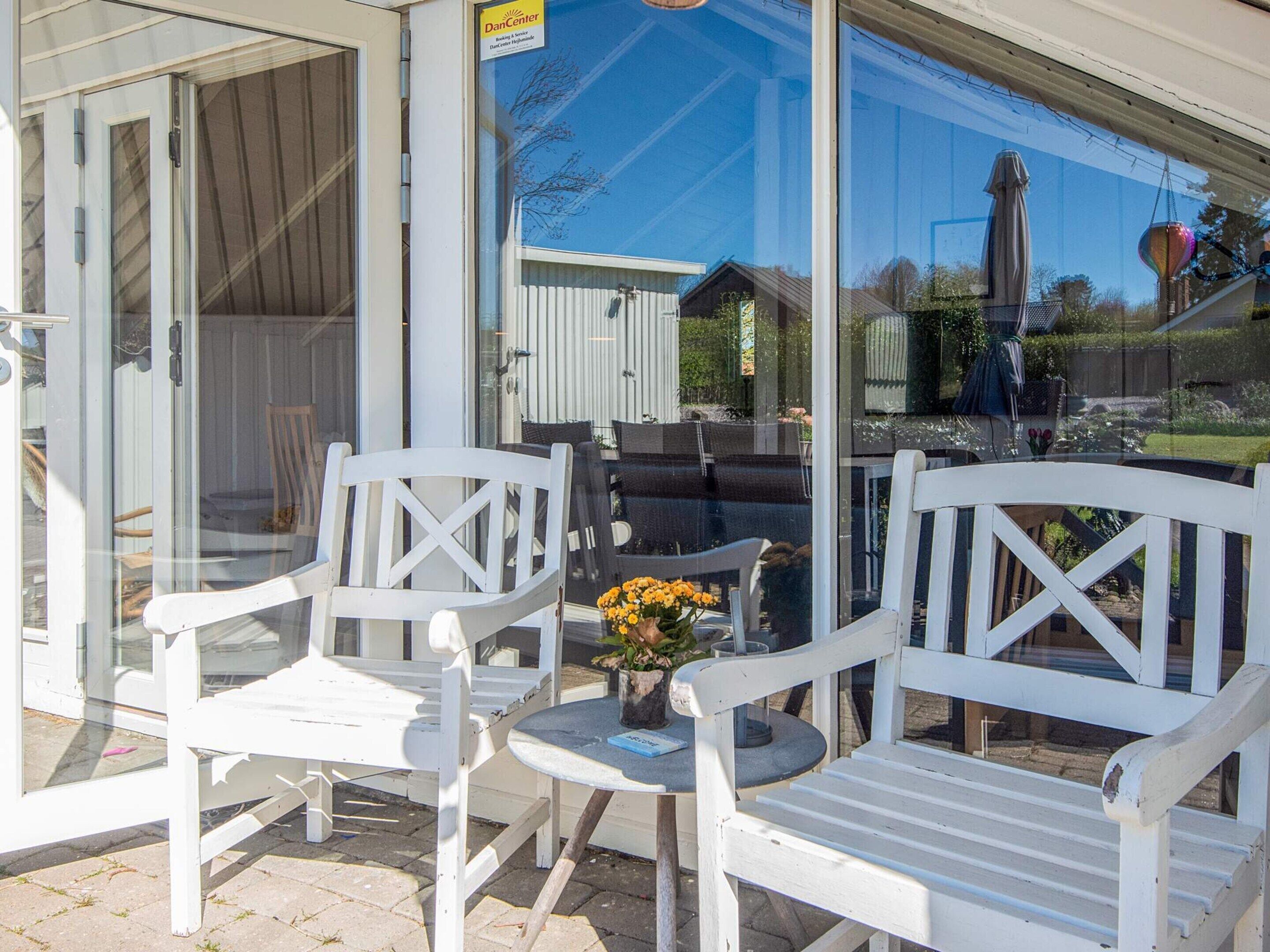 A patio area with white chairs and a table, a glass door, and a view of a house and garden.