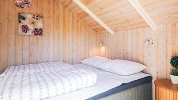 Un dormitorio de cabaña de madera con una cama, dos lámparas fijadas a la pared y dos cuadros con motivos florales.