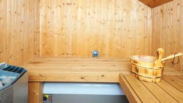 A sauna room with wooden walls, a bench, a bucket, and a control panel.