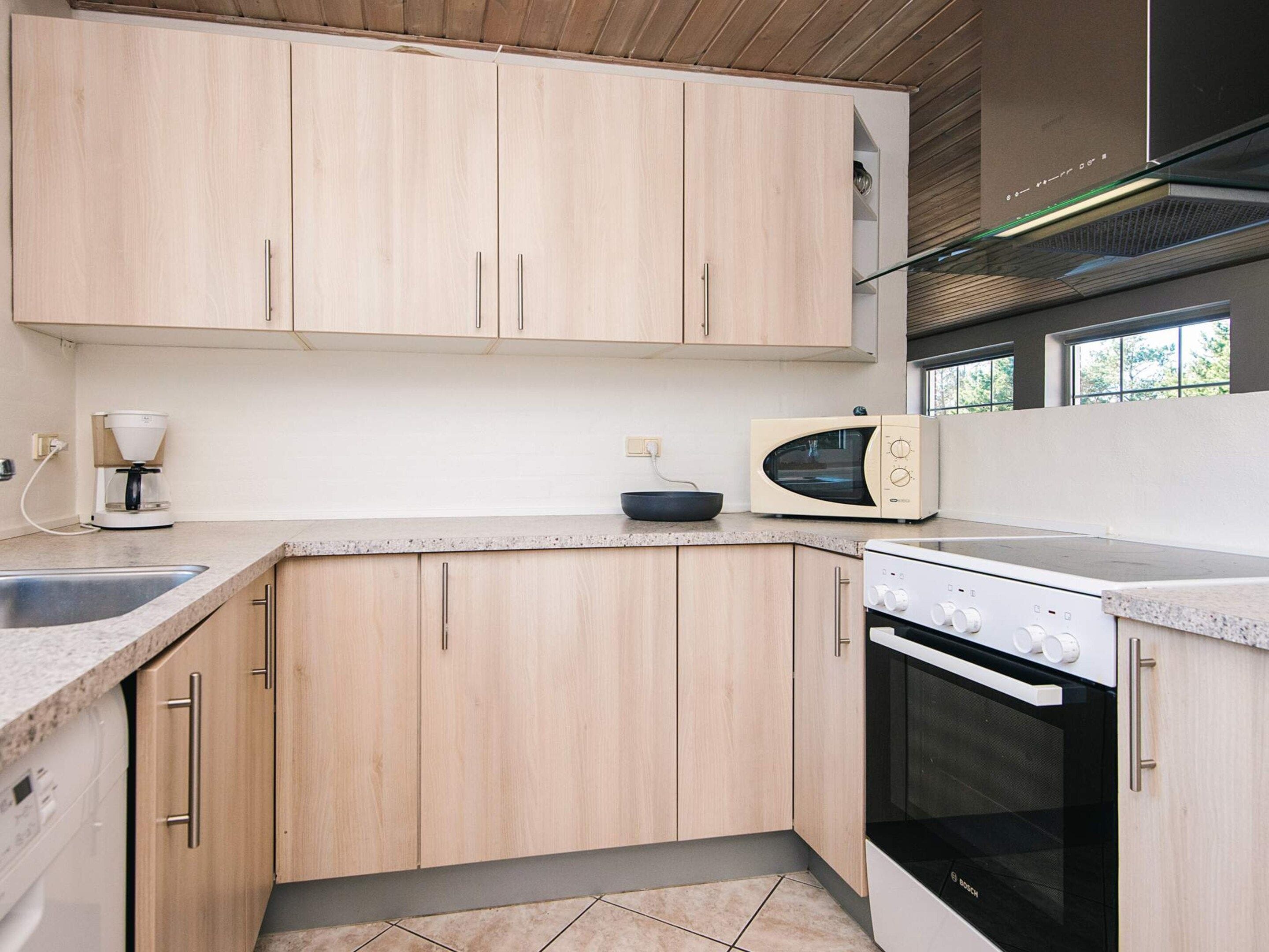 A modern kitchen with light wood cabinets, a built-in microwave, a Bosch oven, and a coffee maker.