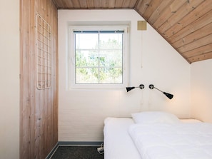 A bedroom with a single bed, a window with a view of greenery, and a slanted ceiling.