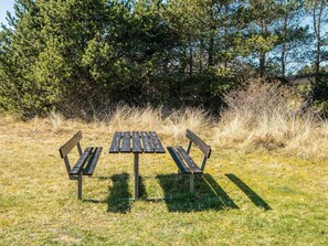 A picnic table with benches in a grassy area with trees in the background.