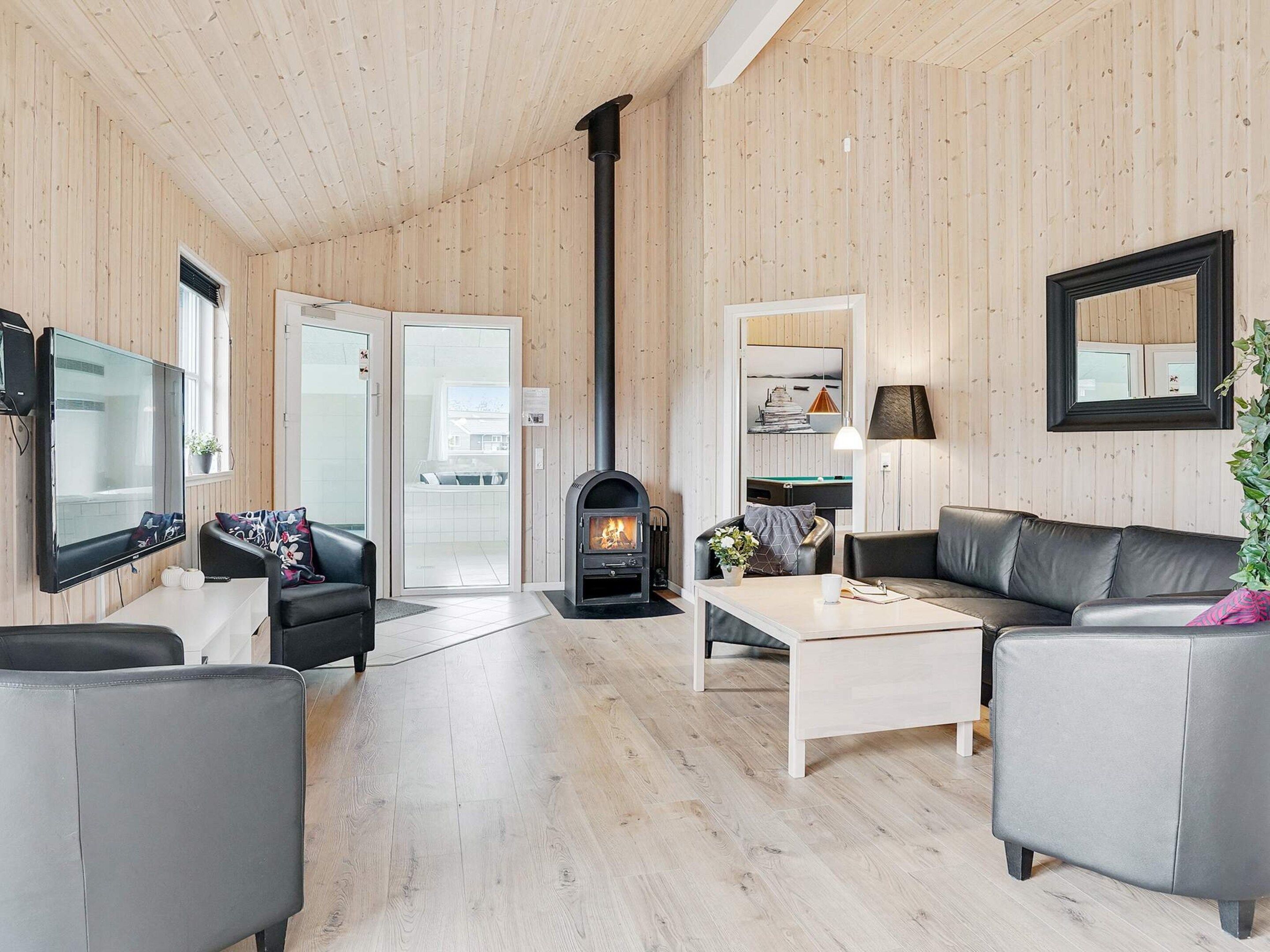 A modern living room with a fireplace, leather sofas, a flat-screen TV, and wooden panel walls.
