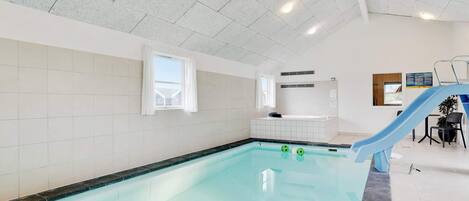 An indoor swimming pool with a blue slide, a jacuzzi, and a small window.