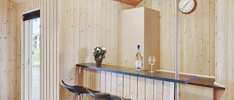 Een houten interieur met een bar, krukken, een klok en een potplant.