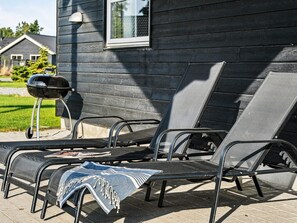 A patio with two lounge chairs, a barbecue grill, and a house in the background.