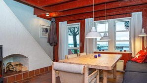 Een knus vertrek met een houten eettafel, stoelen, een bank en een open haard.