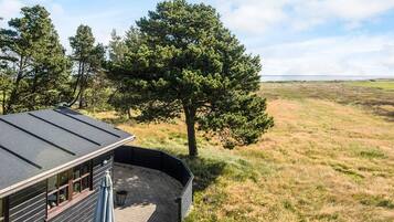 Un edificio con techo curvo, un patio con mesa y sillas, y vista a un campo cubierto de césped y árboles.