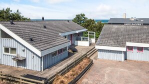A coastal property with a wooden deck, a small building with a red door, and a view of the sea. - 8 Person Holiday Home in Glesborg (Glesborg)