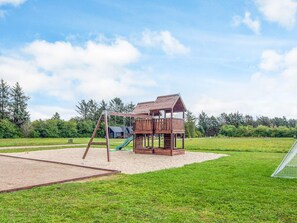 Un parque infantil con una casita de madera, un tobogán y columpios.