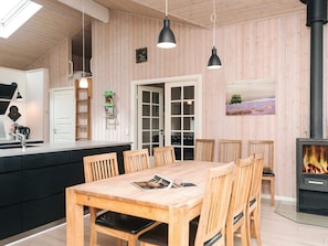 A modern kitchen with wooden walls, a dining area with a wooden table and chairs, a built-in stove, and a large window with a view of the countryside. - 5 Star Holiday Home in Ansager (Ansager)
