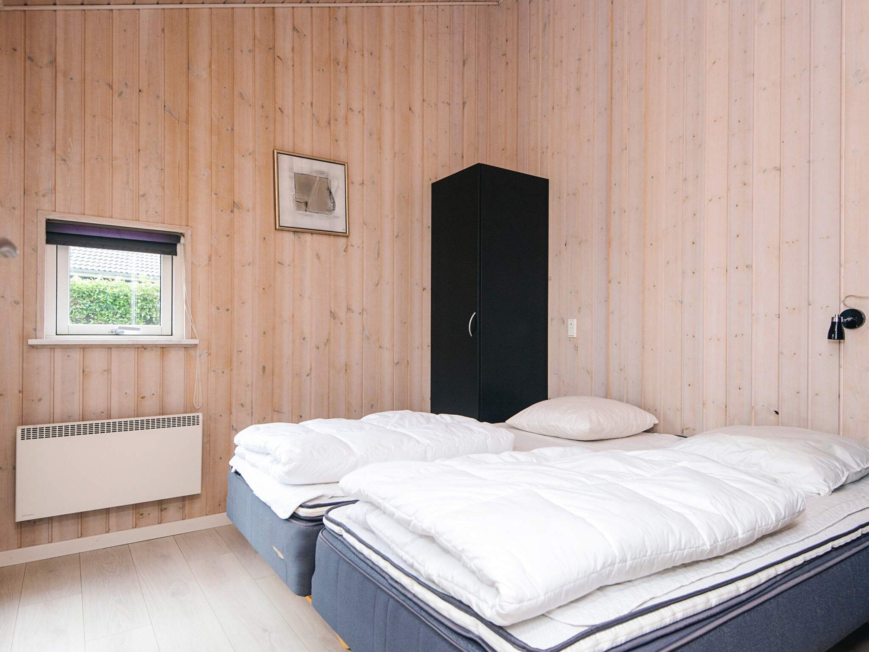 A bedroom with a bed, a wardrobe, a radiator, and a window with a view of greenery.