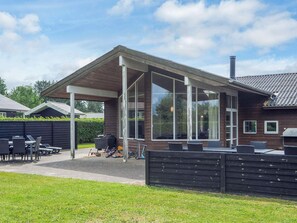 Une terrasse extérieure couverte, équipée d’un barbecue, d’un espace salon et offrant une vue sur le jardin arrière.