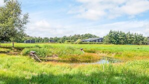 A rural landscape with a pond, grassy fields, and several buildings in the background. - 5 Star Holiday Home in Ansager (Ansager)