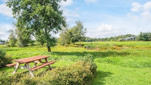 Une table de pique-nique dans un champ herbeux, avec des arbres et des maisons en arrière-plan.