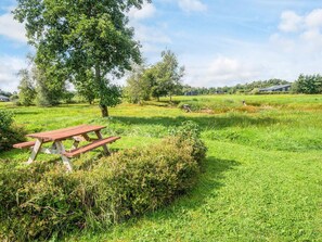A picnic table in a grassy field with trees and houses in the background.