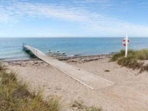 A beach with a wooden walkway leading to the water, a lifeguard sign, and a clear sky. - 5 Person Holiday Home in Rodby-by Traum (Rodby)