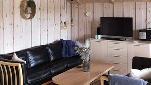 Ein gemütliches Zimmer mit einer schwarzen Ledersofa, einem Holztisch, einem Fernseher und einem kleinen Schreibtisch mit Schubladen.