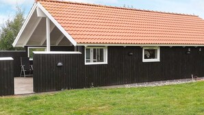 Ein eingeschossiges Gebäude mit rotem Ziegeldach, weißen Fensterrahmen und einer dunklen Holzfassade.