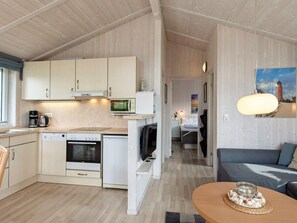 Une cuisine compacte dotée d’appareils électroménagers modernes, un coin repas avec une table et des chaises, et un salon avec un canapé et un tableau.