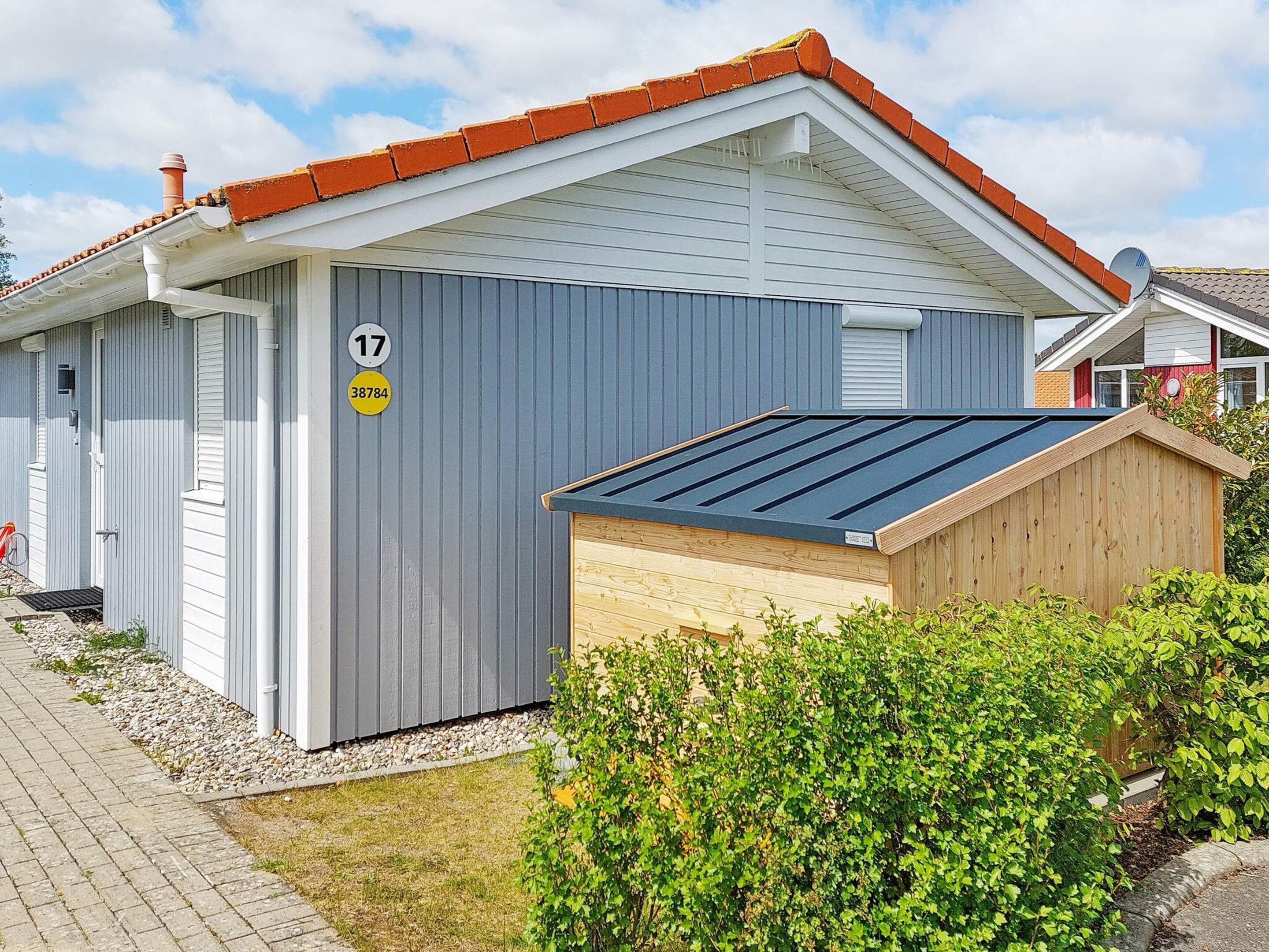 A single-story building with a grey exterior, a red-tiled roof, and a small attached wooden structure.