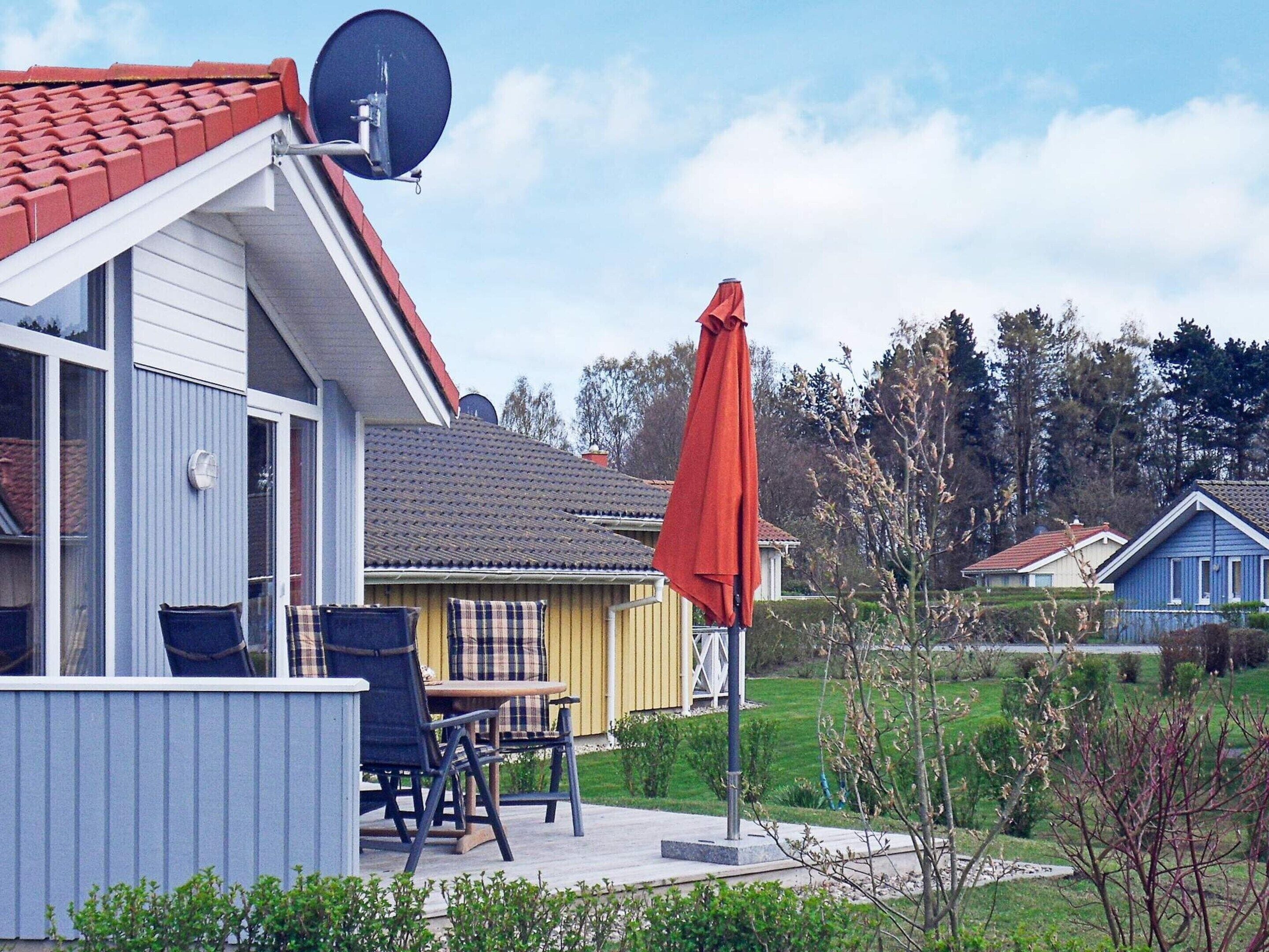 A residential area with a house featuring a satellite dish, a patio with a table and chairs, and a red umbrella.