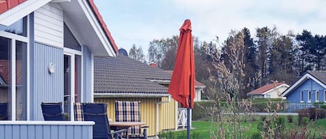 A residential area with a house featuring a satellite dish, a patio with a table and chairs, and a red umbrella.