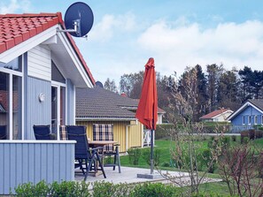 Un quartier résidentiel avec une maison dotée d’une antenne parabolique, d’une terrasse avec une table et des chaises, et d’un parasol rouge.